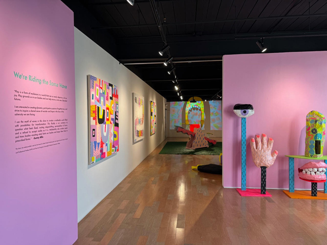 Carberry Gallery front with Riding the We're Riding the Same Wave exhibit. There is a spooky paper mache hand and eye against a bright pink wall.