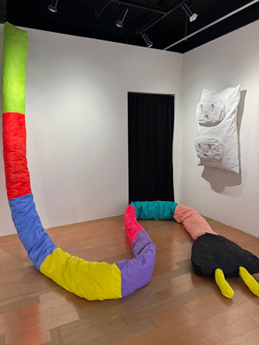 a giant whimsical fabric wall plug snakes on the gallery floor