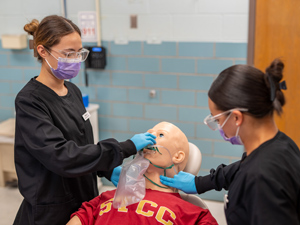 dental hygiene students applying mask to mouth of simulation body